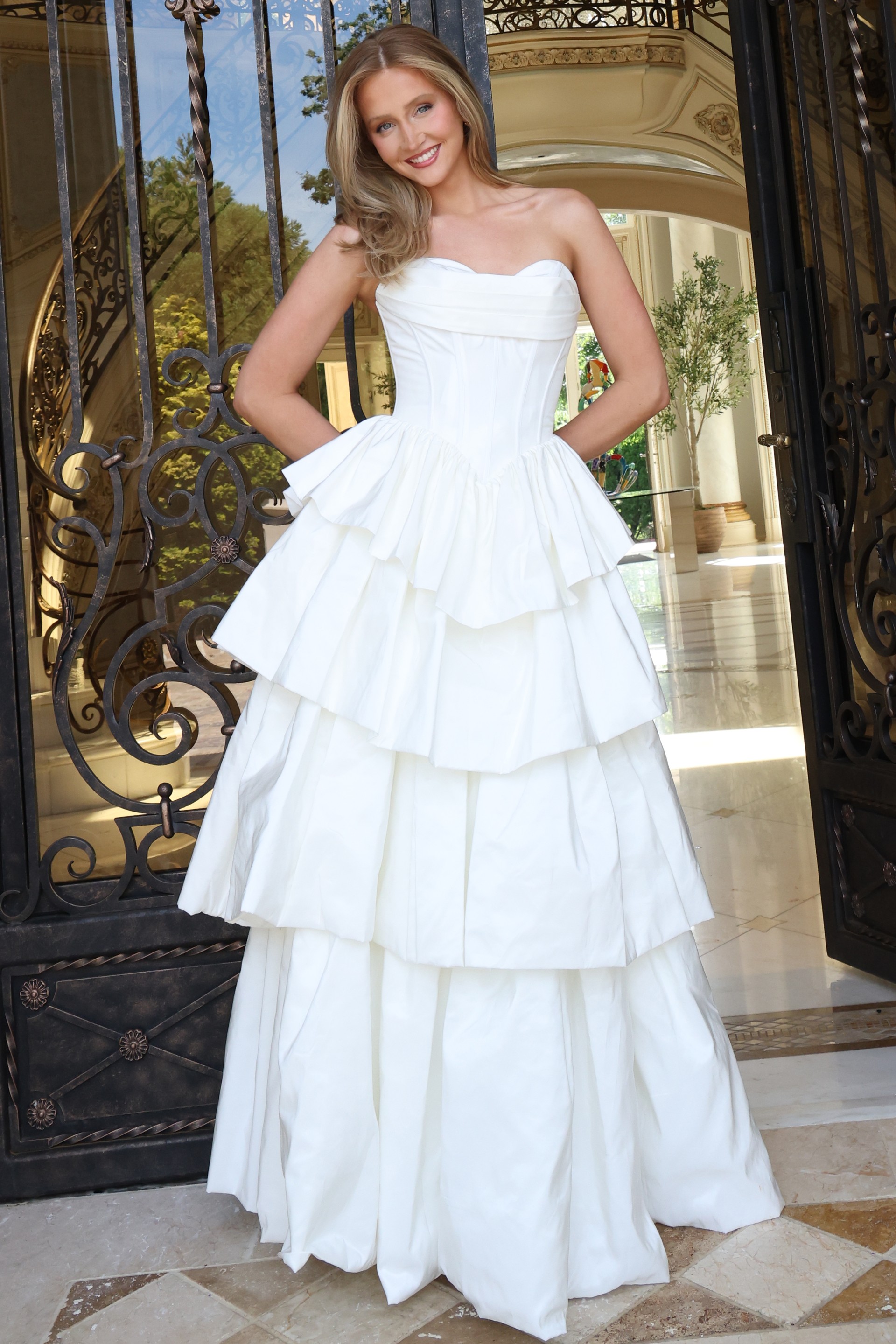 white strapless layered ruffle ball gown - front full body, blonde hair smiling hands behind