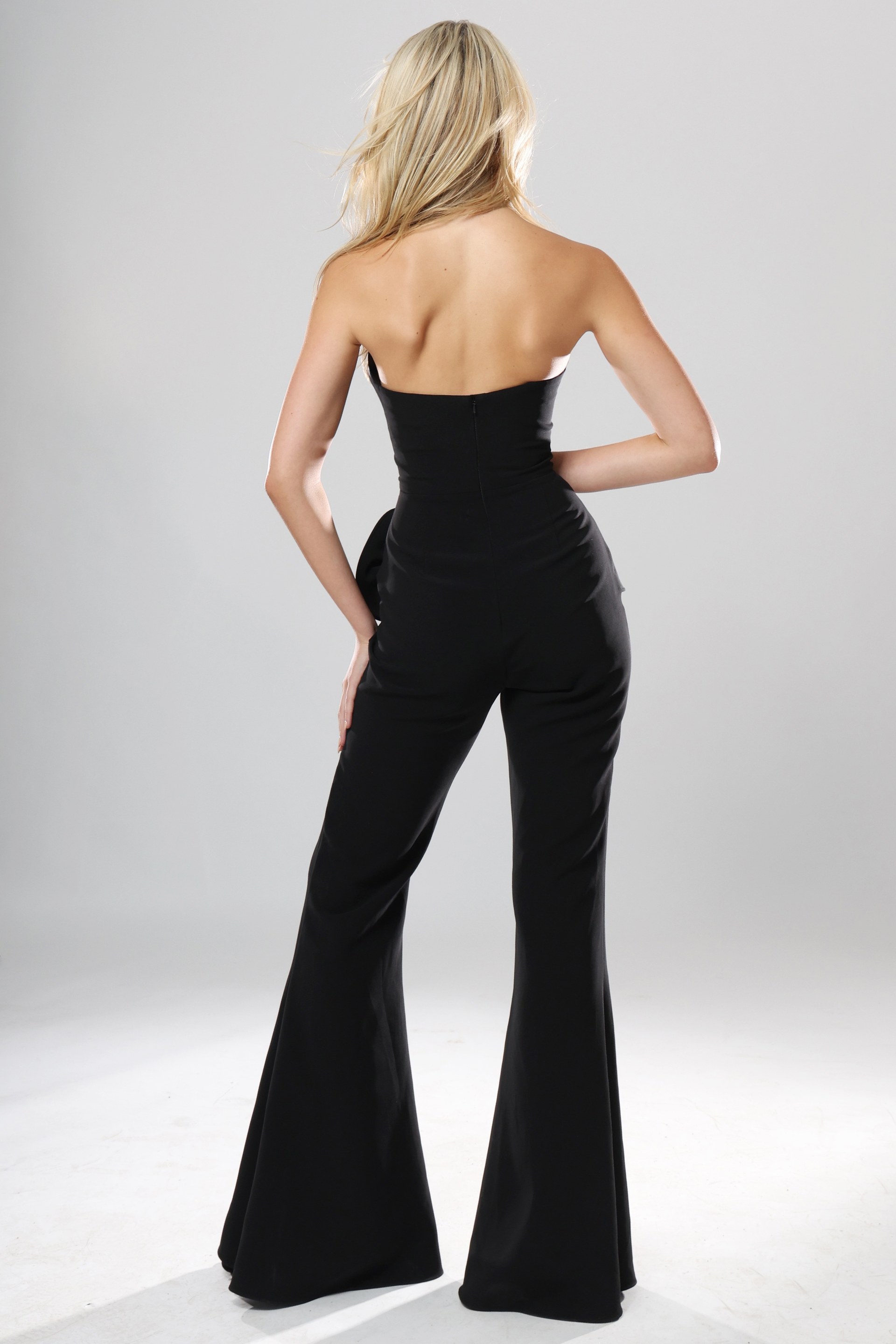 back view of black strapless jumpsuit with straight neckline, peplum rosette detail and wide leg pants, Jovani style 48209