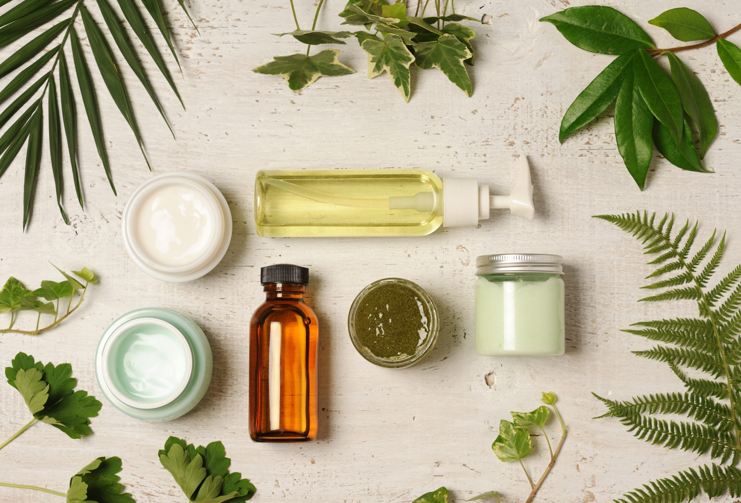Various beauty product containers surrounded by various leaves.