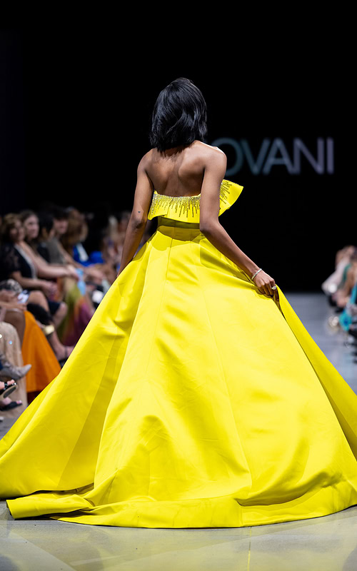 Back view of model wearing Jovani S36369 yellow gown with voluminous skirt