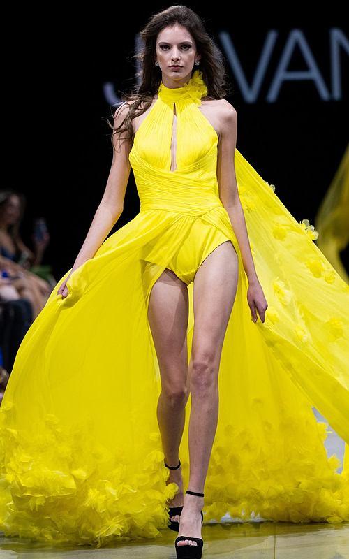 Model wearing Jovani S38104 yellow gown with halter neckline and flowing cape, front view.