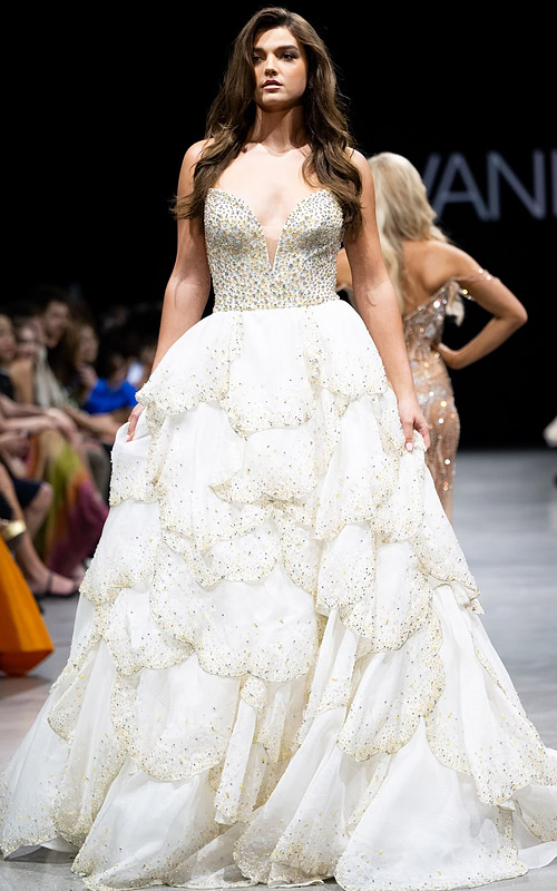 Model wearing Jovani S38886 white gown with deep V-neck and layered skirt, front view